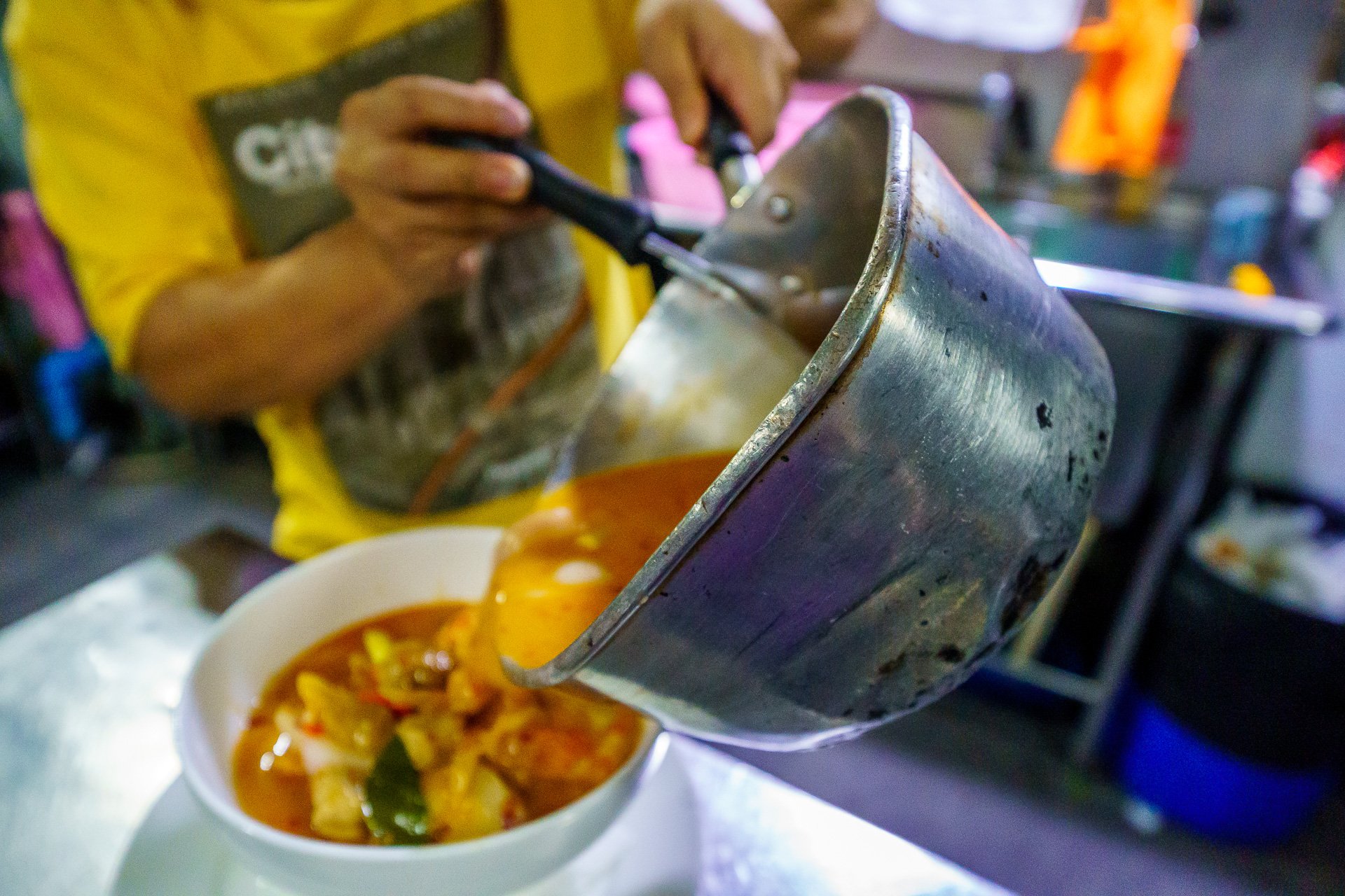 Cook pouring Tom Yum Soup into a bowl in the kitchen oF The Game Bangkok.
