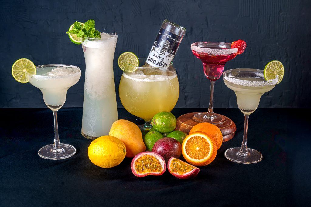 Assortment of margaritas, a mint cocktail, a beer-bottle cocktail and fruit garnishes.