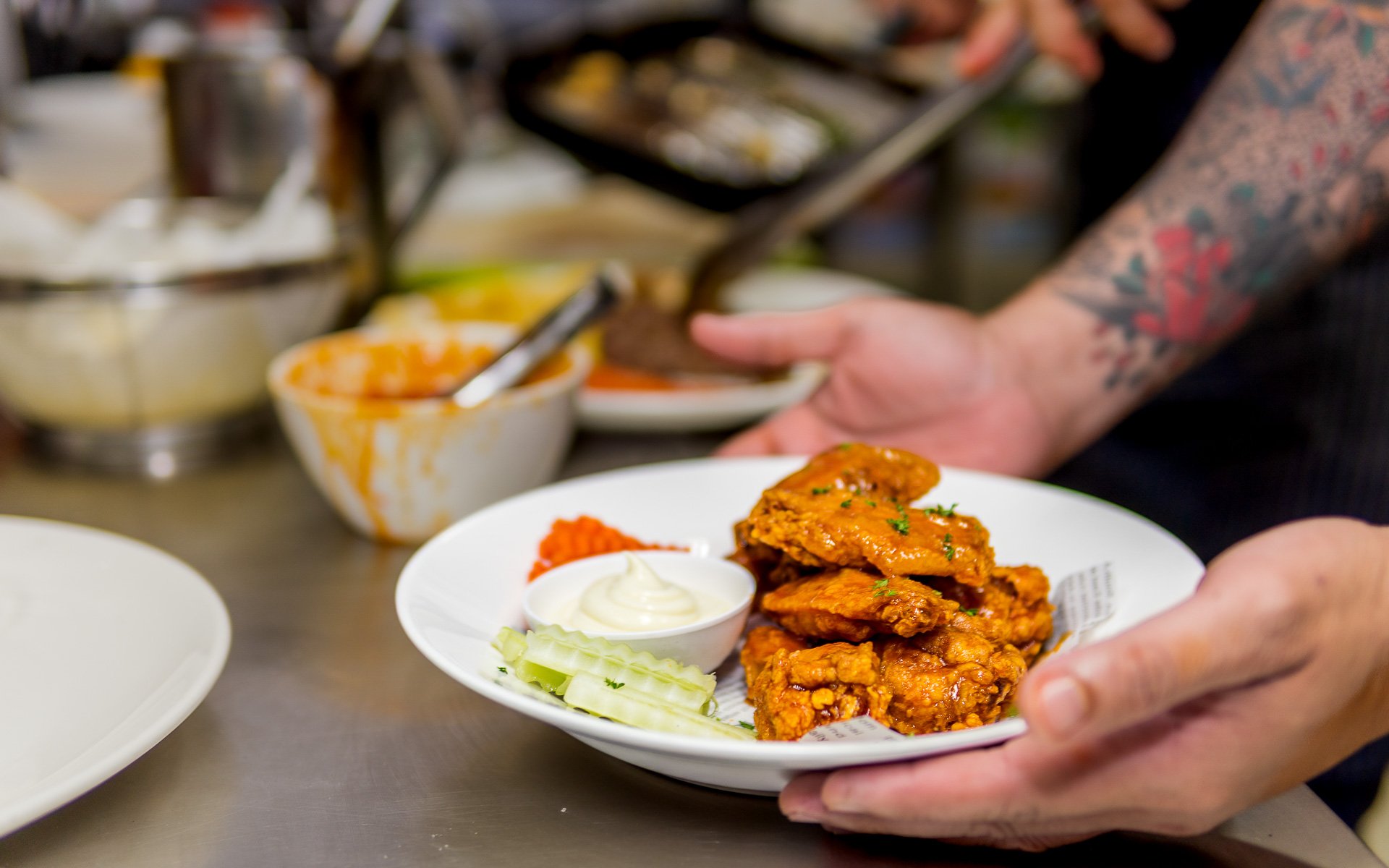 Cook holding a plate of crispy chicken wings with celery and dip.