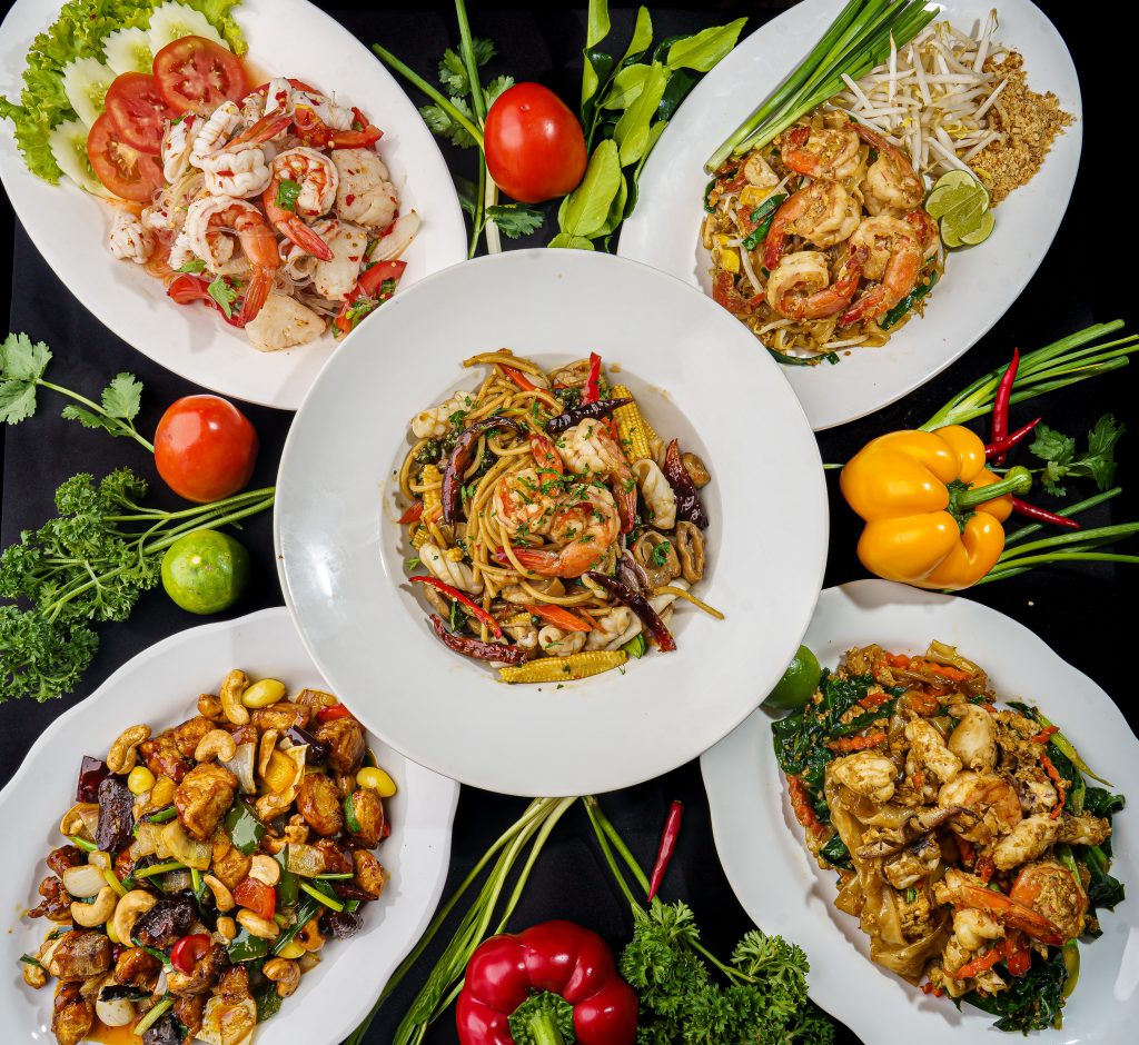 Overhead food photography of Thai seafood dishes including prawn pad Thai, spicy seafood glass-noodle salad and stir-fried noodles.